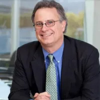 Christopher Mariott smiling, wearing a black suit, blue shirt and printed tie.